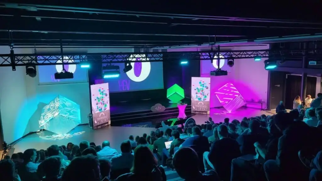 Conférence digitale du Dev Summit ADEO en amphithéâtre : cubes lumineux, roll-ups et public face à la scène